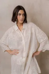 Camisola blanca de silueta amplia y caída liviana, con bordados florales sutiles, cuello camisero, cierre frontal de botones y mangas 3/4.