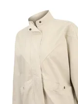 Chaqueta de gabardina color beige RKF modelo Otter, de corte holgado, con cuello alto, cierre frontal con cremallera y solapa con botones a presión. Cuenta con bolsillos frontales con solapa, costuras decorativas en V en el pecho y trabillas ajustables en el ruedo.