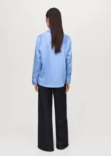 Camisa de corte recto y diseño a rayas verticales, con cuello camisero, cierre frontal de botones y mangas largas con puños abotonados.