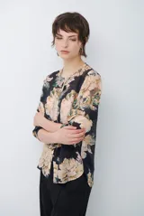 Camisa de manga larga con fondo verde y estampado floral en tonos rosados y beige, cuello redondo con pequeña abertura en V y cierre frontal con botones.