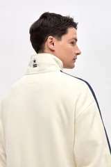 Campera de felpa con friza, de corte relajado, color negro con detalles en bordó. Presenta cuello alto, cierre frontal metálico, bolsillos laterales y cintas decorativas a contratono en las mangas.