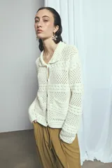 Cardigan de punto calado color marfil, con cuello solapa, cierre frontal de botones oscuros y bolsillos frontales.
