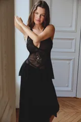 Falda de tiro bajo color negro, confeccionada en hilatura de viscosa. Presenta detalles de bordados y aplicación de puntilla a tono en la parte superior. El bajo tiene un acabado asimétrico con volados de gasa y cuenta con forro interior. El cierre es lateral con botones forrados.