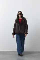Campera tipo gamulán de símil cuero color marrón oscuro, con interior y solapas de corderito al tono. Presenta cierre frontal cruzado, bolsillos con cierre metálico y hebilla ajustable en el cuello.