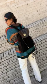 Mochila Brassy confeccionada en combinación de gamuza marrón oscuro y cuero negro, con solapa de cuero texturado y herrajes metálicos en tono oro viejo. Presenta correas regulables y diseño funcional para el día a día.
