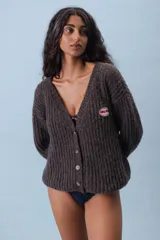 Cardigan de punto grueso color gris oscuro, con escote en V, cierre frontal de botones y parche decorativo en el pecho. Presenta mangas largas con puños ajustados.