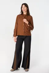 Camisa de color camel con textura geométrica en relieve, cuello clásico y cierre frontal con botones. Presenta mangas largas con detalle de tiras ajustables y aberturas en los puños.