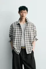 Camisa relaxed fit confeccionada en tejido de mezcla de algodón con textura irregular, diseño a cuadros en tonos gris, marrón y blanco, con cuello solapa, manga larga con puño abotonado, bolsillo de parche en el pecho y cierre frontal con botones.