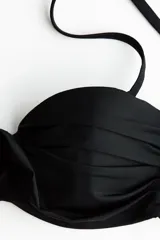 Top de bikini balconette negro con copas acolchadas, aros, varillas laterales y detalle girado en el centro. Incluye tirantes ajustables y extraíbles.
