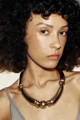 Collar de cordón negro con nudos y piezas metálicas doradas de diferentes formas y tamaños, con cierre ajustable mediante pieza circular.