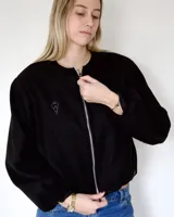Campera bomber negra con cierre frontal plateado, cuello redondo y mangas largas con puños elastizados. Presenta un pequeño bordado en el pecho.