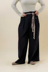Pantalón wide leg de tiro alto en color negro, con diseño de pinzas delanteras que aportan volumen y caída fluida. Incluye bolsillos laterales y un lazo desmontable en la cintura que combina cordón con cinta de estampado animal print.