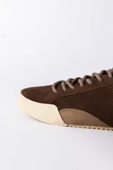 Championes urbanos de gamuza color marrón, con suela de goma en tono crema y cordones jaspeados. Presenta un refuerzo en la puntera y un detalle en cuero beige en el talón.