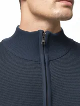 Campera tejida de punto con cierre frontal completo, cuello medio y dos bolsillos laterales abiertos. Presenta un diseño de textura en relieve y puños acanalados.