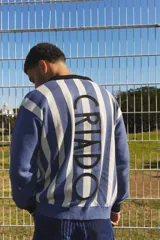 Buzo de punto estilo retro inspirado en la camiseta de la selección de 1930, con diseño de rayas verticales en azul y blanco. Presenta cuello polo negro, puños a contratono y la palabra 'CRIADO' bordada en letras grandes sobre la espalda.