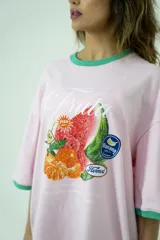 Remera oversize rosa con cuello y mangas con ribete verde. Estampado frontal con diseño de frutas y texto.