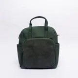 Mochila de diseño versátil en color verde, confeccionada con una combinación de texturas. Presenta un cuerpo principal de cuero sintético texturizado y un bolsillo frontal amplio de gamuza. Incluye manijas superiores para llevar en la mano, bolsillos laterales abiertos y cierre principal con cremallera.