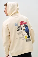 Canguro beige con capucha, cordones ajustables y bolsillo tipo canguro. Estampado en el pecho con el logo de DTMF y en la espalda con un diseño alusivo al álbum "Un Verano Sin Ti" de Bad Bunny.