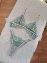 Conjunto de lencería compuesto por un bralette triangular y una bombacha tipo tanga, confeccionados en encaje color verde oliva con detalles y elásticos en tono tostado.