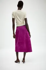 Falda midi de tiro medio tipo pareo confeccionada en piel. Presenta un diseño cruzado con cierre frontal y bajo asimétrico.