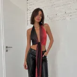 Top halter con diseño bicolor en negro y rojo, confeccionado en tela brillante con efecto degradado. Presenta un escote profundo en V y un nudo frontal con caída larga.