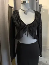 Top de tul negro con mangas largas, escote profundo con volados y cierre frontal con lazo para anudar.