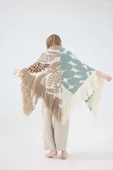 Ruana triangular tejida en lambswool, con diseño bicolor que combina un lado con estampado botánico en tonos tostado y marrón, y el otro lado en color verde claro con formas abstractas. Cuenta con terminación de flecos en los bordes.
