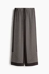 Pantalón de tiro alto con cintura elástica, piernas rectas y diseño estampado de líneas blancas que forman un marco geométrico en la parte inferior sobre fondo negro.
