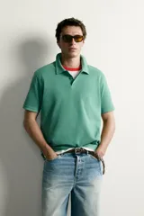 Remera polo regular fit de color gris oscuro, confeccionada en tejido de algodón con textura de rayas verticales. Cuenta con cuello solapa, cierre frontal con botones y mangas cortas con terminación en rib.