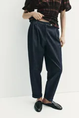 Pantalón chino de tiro medio confeccionado en denim oscuro. Presenta pinzas en el delantero, bolsillos laterales y bajo con acabado en vuelta. Cierre frontal con cremallera y botón.