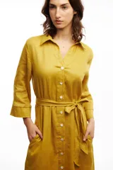 Vestido camisero midi color mostaza confeccionado en lino, con cuello camisero, botones frontales de nácar, mangas 3/4 y lazo en la cintura.