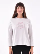 Remera de manga larga color crema con cuello redondo y un estampado central de un ramo de flores rosadas y naranjas en un jarrón azul oscuro.