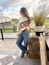 Sweater de punto color crema con diseño geométrico en tonos marrones, naranjas, verdes y grises en el pecho y las mangas. Confeccionado con lana y cuero, con detalles tejidos y bordados a mano.