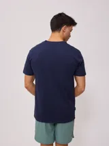 Remera color crema de manga corta con estampado frontal con el texto "Rusty Supply Surfboards" en color rojo y negro.