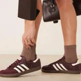 Championes Adidas Samba OG de color bordó con textura símil piel de serpiente y detalles en blanco marfil. Cuentan con las clásicas tres tiras laterales, inscripción 'SAMBA' en letras doradas, refuerzo de gamuza en la puntera y suela de goma marrón.