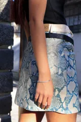 Minifalda con estampado de piel de serpiente en tonos celeste y blanco, con pretina ancha color crudo y cinturón fino negro.