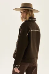 Campera de lana merino hervida en color crudo, con diseño de cuello camisero, cierre frontal de botones y bolsillos frontales. Presenta bordados artesanales con motivos geométricos en tonos marrón y azul en el frente, espalda y mangas.