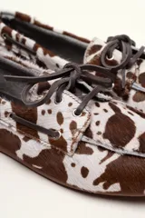 Mocasín tipo boat shoe color marrón, confeccionado en cuero, con cordones de cuero marrón y cordones decorativos azules.