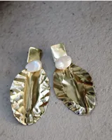 Par de aros colgantes con base rectangular y dije en forma de hoja texturizada color dorado, con perla irregular blanca. Cierre a presión.