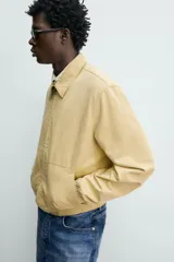 Cazadora regular fit de color beige, confeccionada en mezcla de algodón y lyocell. Cuenta con cuello camisero, cierre frontal de cremallera, bolsillos de plastrón en la cadera, mangas largas con puños elásticos y bajo con ajuste elástico.