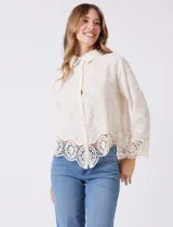 Camisa de algodón con bordado suizo, cuello con solapa y cierre frontal con botones. Presenta mangas largas con terminación de encaje calado y un ruedo asimétrico en pico con un amplio galón de encaje.