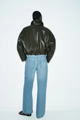 Chaqueta estilo bomber de efecto piel en color verde oliva, con cuello solapa, cierre frontal con cremallera, mangas largas y bajo elástico.