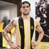 Musculosa de básquet Puma del Peñarol, modelo Third 2025. Diseño en color tostado con dos franjas verticales negras y amarillas en el centro, con el logo de Puma y el escudo del club bordados.
