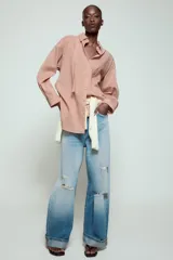 Camisa de cuello solapa y manga larga con estampado de rayas verticales. Presenta un bolsillo de plastrón en el delantero, cierre frontal con botones y detalle de botones en la espalda. Su diseño cuenta con un bajo asimétrico y aberturas laterales.