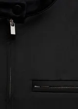 Chaqueta corta de diseño recto, color negro, con cuello de tira, cierre frontal con cremallera, bolsillos laterales y un bolsillo de ribete en el pecho.