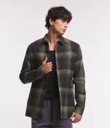 Camisa de corte regular y manga larga, confeccionada en algodón con estampa de cuadros en tonos verde militar y negro. Posee cuello camisero, cierre frontal con botones y un bolsillo aplicado en el pecho con etiqueta de la marca.