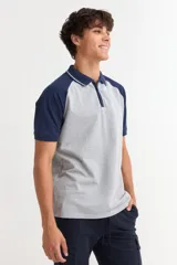 Remera tipo polo de manga corta con diseño combinado, cuerpo en color gris y mangas y cuello en color azul marino. Presenta cierre frontal con botones y detalles de líneas finas en el cuello.