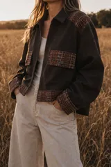 Campera corta de gamuza color marrón oscuro con detalles en tejido de punto tipo tweed en hombros, bolsillos frontales, puños y ruedo. Posee cierre frontal y cuello camisero.