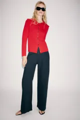 Chaqueta de punto color rojo, con cuello solapa y manga larga. Cierre frontal con fila de botones negros en contraste que se extienden también sobre el cuello.