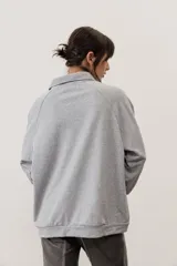 Buzo celeste de manga larga con cuello polo y cierre frontal de botones. Presenta un parche marrón bordado en el pecho.